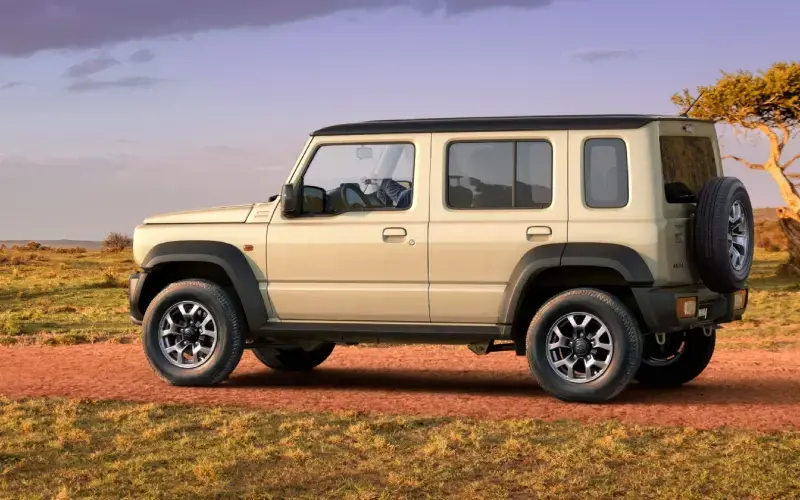 Suzuki Jimny beige conduciendo por una sabana africana con rinocerontes en el fondo.